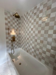 Bath installation with checkerboard beige and white tiles and brass rain shower in South London
