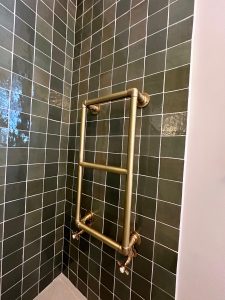 Brass ladder towel rail fitted on dark green tiled wall in South London bathroom renovation