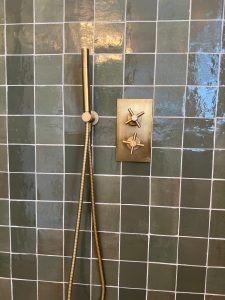 Brass cross-handle shower controls on glossy green zellige tiles in South London bathroom