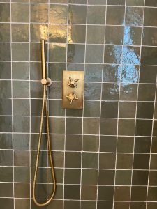 Brushed brass thermostatic shower valve installed on dark green square tiles in South London bathroom