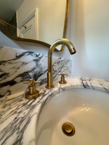 Close-up of brass three-hole basin tap on veined marble countertop in South London bathroom renovation