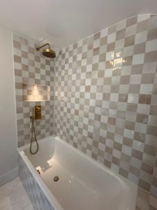 Bath with checkerboard zellige tiles, recessed niche and brass overhead shower in South London bathroom refit