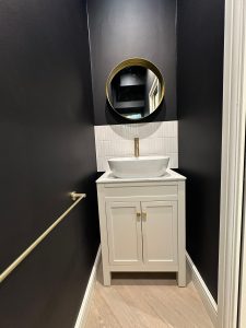 Compact cloakroom with dark walls, white vessel sink, brass tap and round brass mirror in South London