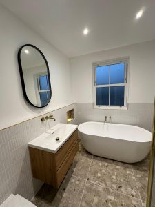 Bathroom renovation with freestanding bath, terrazzo floor tiles and oak floating vanity photographed at dusk in South London