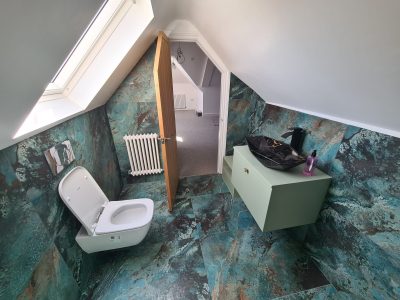 Loft bathroom renovation with full teal and copper effect floor-to-ceiling tiles and wall-hung toilet in South London