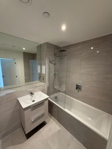Modern bathroom renovation with grey stone tiles, overhead rain shower and white vanity unit in South London