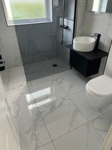 Walk-in shower with marble effect tiles, black vanity unit and vessel basin installed in South London