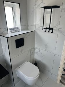 Wall-hung toilet with large marble effect tiles and black steel fixtures in South London bathroom renovation