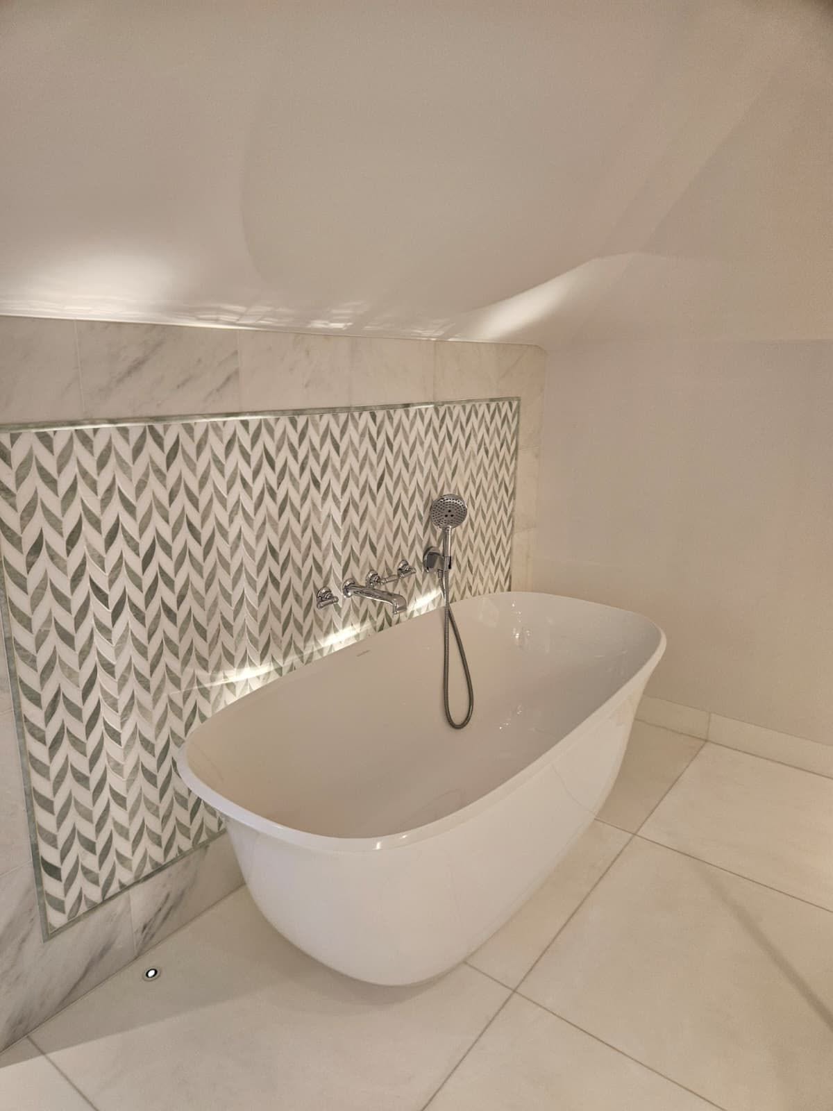 A freestanding bath set against a herringbone feature tile — a traditional bath remains the strongest format for family-target homes.